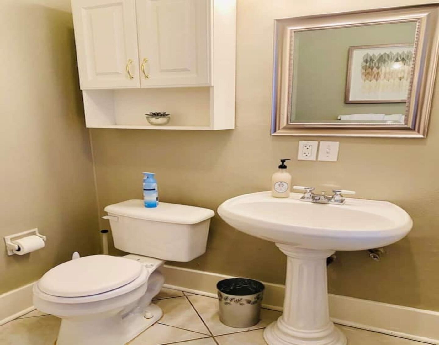 A bathroom with a toilet, sink, and a framed mirror on the wall.