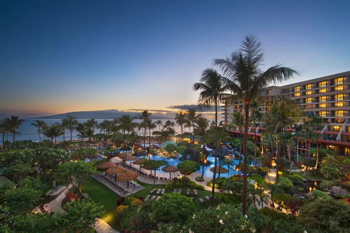 A resort with multiple swimming pools, palm trees, and a view of the ocean.