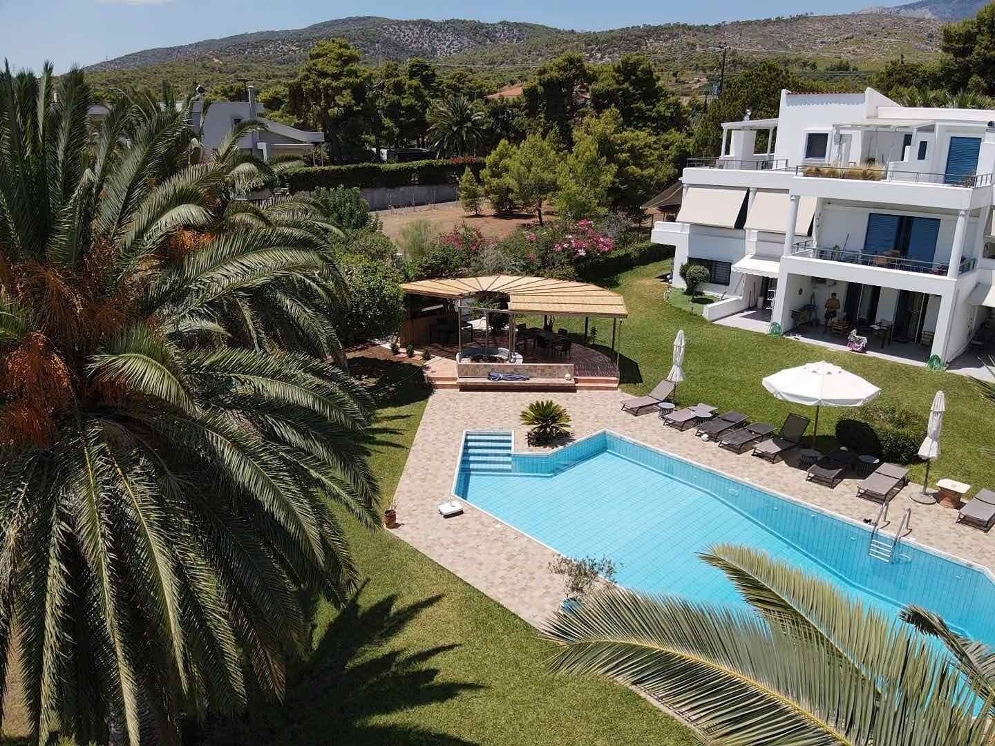En moderne bygning i to etager med swimmingpool, liggestole og et overdækket udendørs opholdsområde.