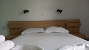 A neatly made bed with white linens and two wall-mounted lamps. - Kinetious Nisous Stylish Apt, Pool, near the Beach (Kineta)