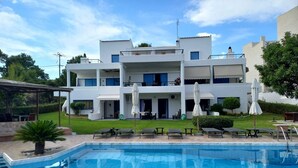 A modern hotel with a swimming pool, multiple balconies, and outdoor seating areas. - Kinetious Nisous Stylish Apt, Pool, near the Beach (Kineta)
