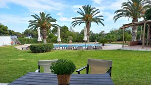 A patio area with a table and chairs, a small potted plant, and a pool in the background. - Kinetious Nisous Stylish Apt, Pool, near the Beach (Kineta)