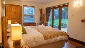 A bedroom with a large bed, wooden wardrobe, bedside lamp, and a view of the garden through a sliding door.