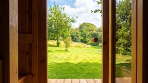 An open wooden door leading to a grassy outdoor area with trees and a clear sky.