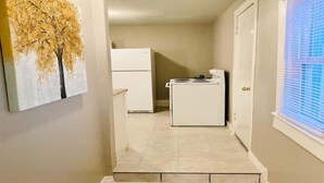 Un couloir menant à une cuisine équipée d’un réfrigérateur et d’un lave-linge.