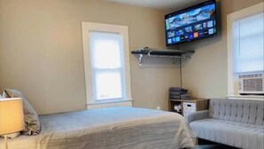 Une chambre d’hôtel avec un lit, un canapé, un téléviseur fixé au mur et une fenêtre avec des stores.