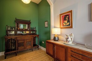 Une pièce avec un mur vert, des meubles en bois, une lampe et un tableau encadré.