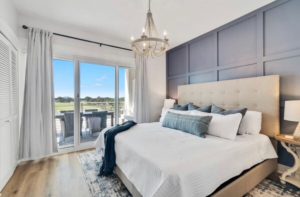 A bedroom with a large bed, a chandelier, a view through the window, and a balcony. - KIVA ON THE GULF: PRIVATE BEACH, PREMIER GOLF COURSE, AND 3 POOLS! (Gulf Shores)