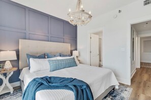A bedroom with a large bed, a chandelier, and a blue accent wall. - KIVA ON THE GULF: PRIVATE BEACH, PREMIER GOLF COURSE, AND 3 POOLS! (Gulf Shores)