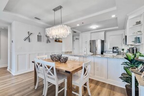 A modern kitchen with white cabinetry, a wooden dining table, and a chandelier. - KIVA ON THE GULF: PRIVATE BEACH, PREMIER GOLF COURSE, AND 3 POOLS! (Gulf Shores)