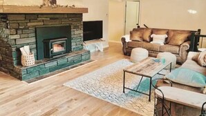 Ein Wohnzimmer mit Kamin aus Stein, einer Sofagarnitur, einem Couchtisch und einem gemusterten Teppich.