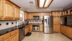 A kitchen with wooden cabinets, a stainless steel refrigerator, a microwave, and a dishwasher. - Riverfront Home w/ Fishing Pier, Minutes to Beach (Matagorda)