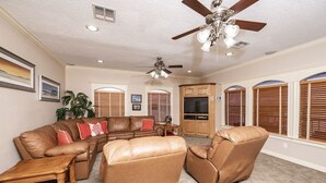 A spacious living room with leather furniture, a ceiling fan, and large windows with blinds. - Riverfront Home w/ Fishing Pier, Minutes to Beach (Matagorda)