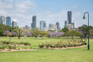 A park with manicured lawns and flower beds, surrounded by a city skyline with modern buildings.