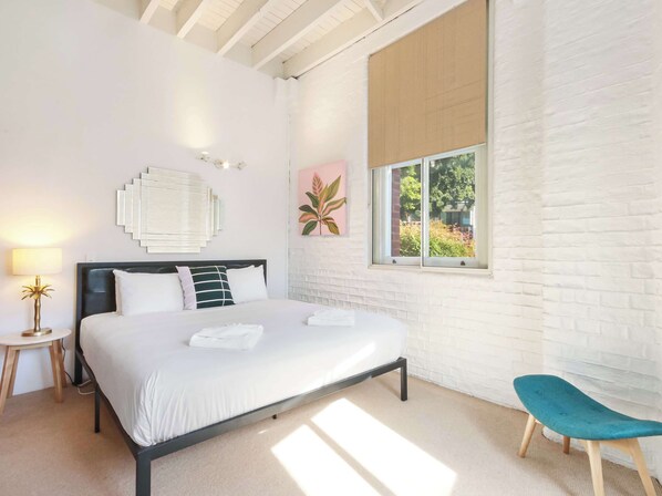 A modern bedroom with a bed, bedside table, lamp, and a window with a view of greenery.
