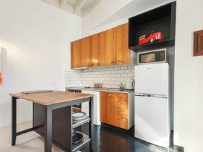 A compact kitchen with wooden cabinets, a white tiled backsplash, a microwave, and a refrigerator.