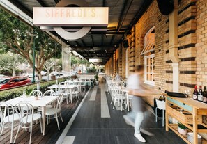An outdoor dining area with tables and chairs, a brick wall, and a sign reading 'Siffredi's'.