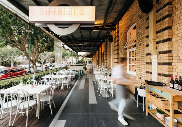 Un espace extérieur aménagé pour les repas, avec des tables et des chaises, un mur en briques et une enseigne portant l’inscription « Siffredi’s ».