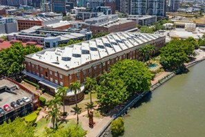 A large, rectangular building with a flat roof, surrounded by greenery and a river.