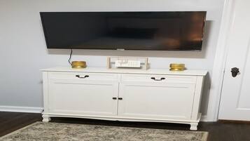 Un meuble blanc à deux tiroirs, un téléviseur à écran plat fixé au-dessus, et un tapis à motifs sur le sol.