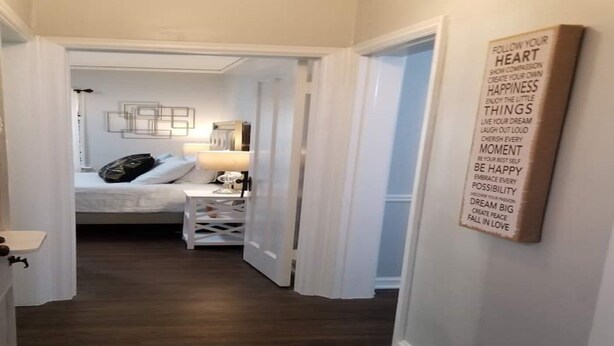 Un pasillo que conduce a un dormitorio con cama, mesita de noche y una cita motivacional en la pared.
