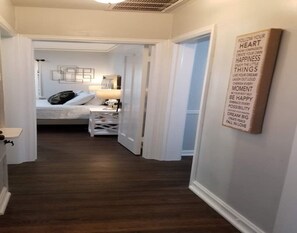 Un pasillo que conduce a un dormitorio con cama, mesita de noche y una cita motivacional en la pared.