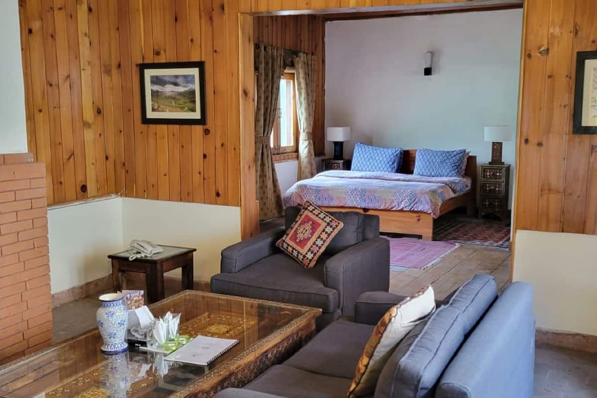 A room with a fireplace, a bed with patterned bedding, a sofa, and a coffee table with a vase and papers.