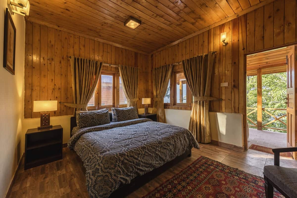 A wooden-paneled bedroom with a large bed, two bedside tables, and a view of the outdoors.
