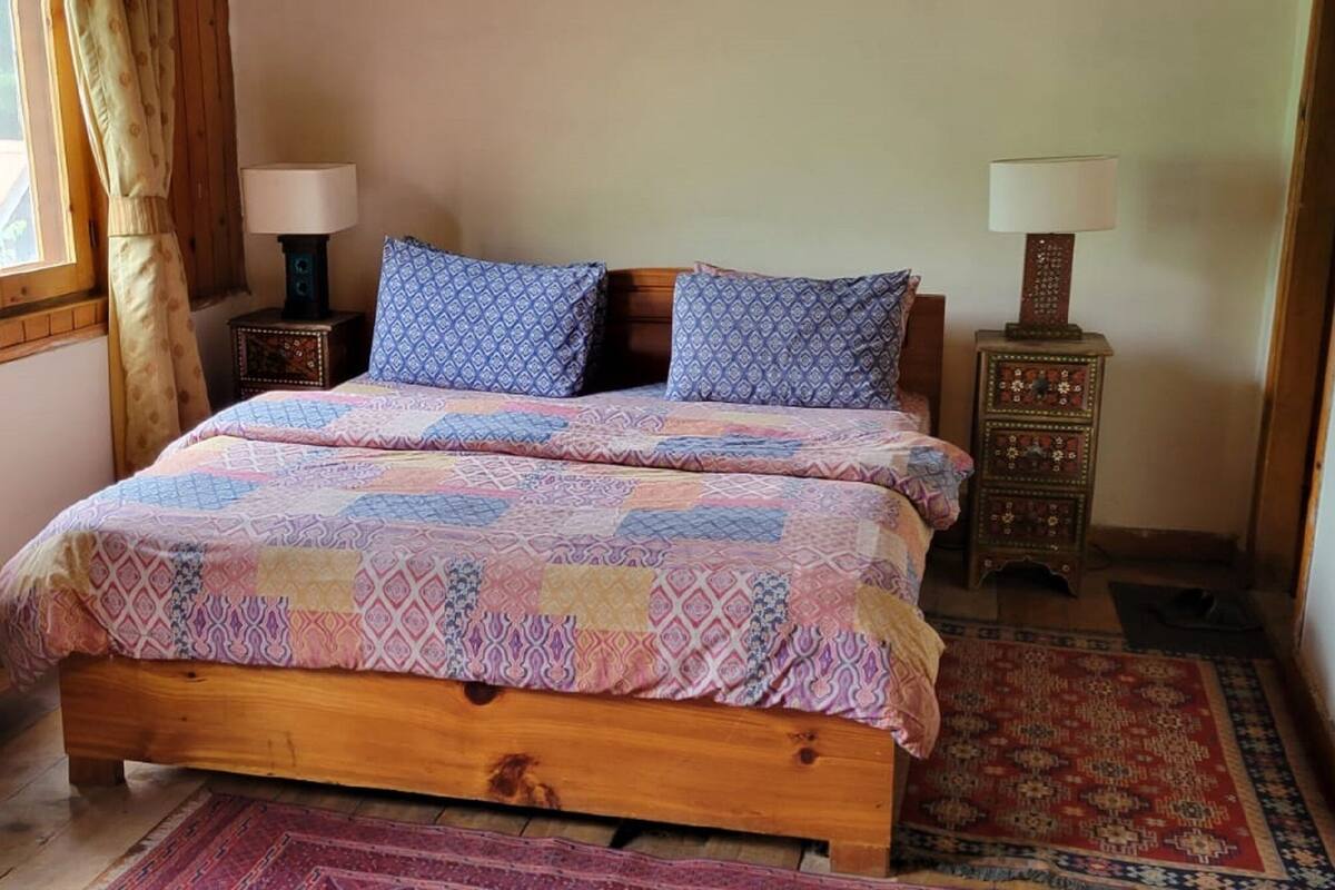 A wooden bed with patterned bedding, two bedside lamps, and a rug.