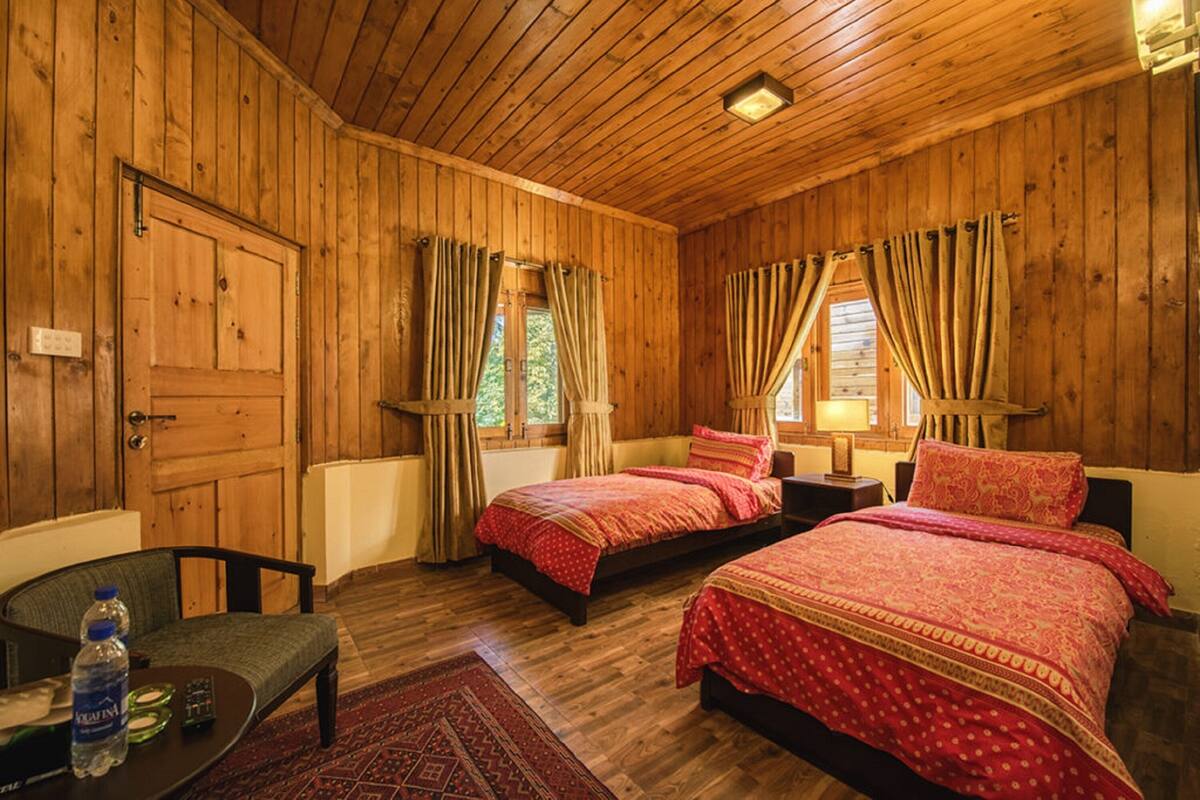 A wooden room with two beds, a table, and a chair.