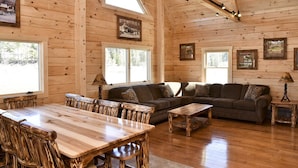 A wooden cabin interior with a dining table, chairs, a sofa, and a coffee table. - Stay on Kingdom Trails in a four bedroom cabin! (Burke)