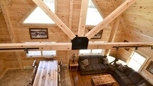 A wooden cabin interior with a dining table, sofa, and a large window. - Stay on Kingdom Trails in a four bedroom cabin! (Burke)