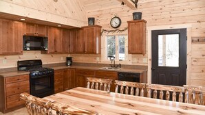 A wooden cabin kitchen with a large dining table, built-in cabinets, a stove, and a sink. - Stay on Kingdom Trails in a four bedroom cabin! (Burke)