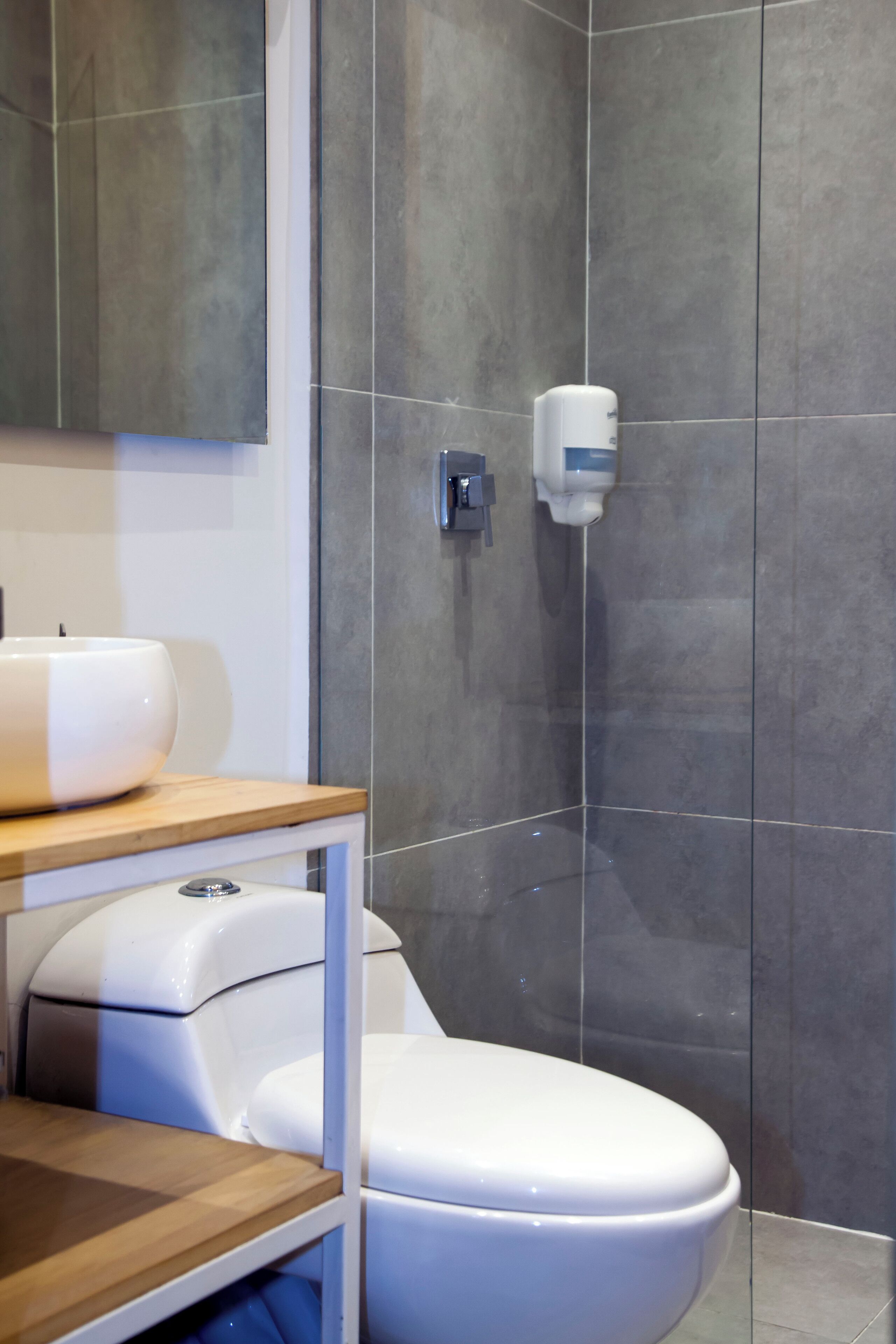A modern bathroom with a white toilet, a wooden vanity, and a glass shower enclosure.