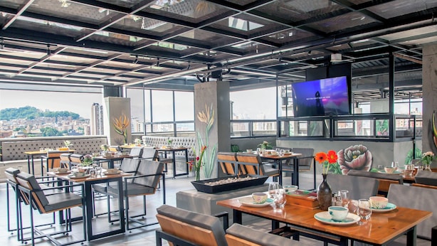 A modern restaurant with high ceilings, large windows, and a city view. Tables are set with dishes and drinks. - Edificio Helena (Medellín)