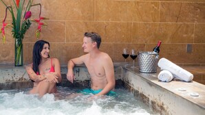 A man and a woman in a hot tub with a vase of flowers and a bottle of champagne on the side. - Edificio Helena (Medellín)