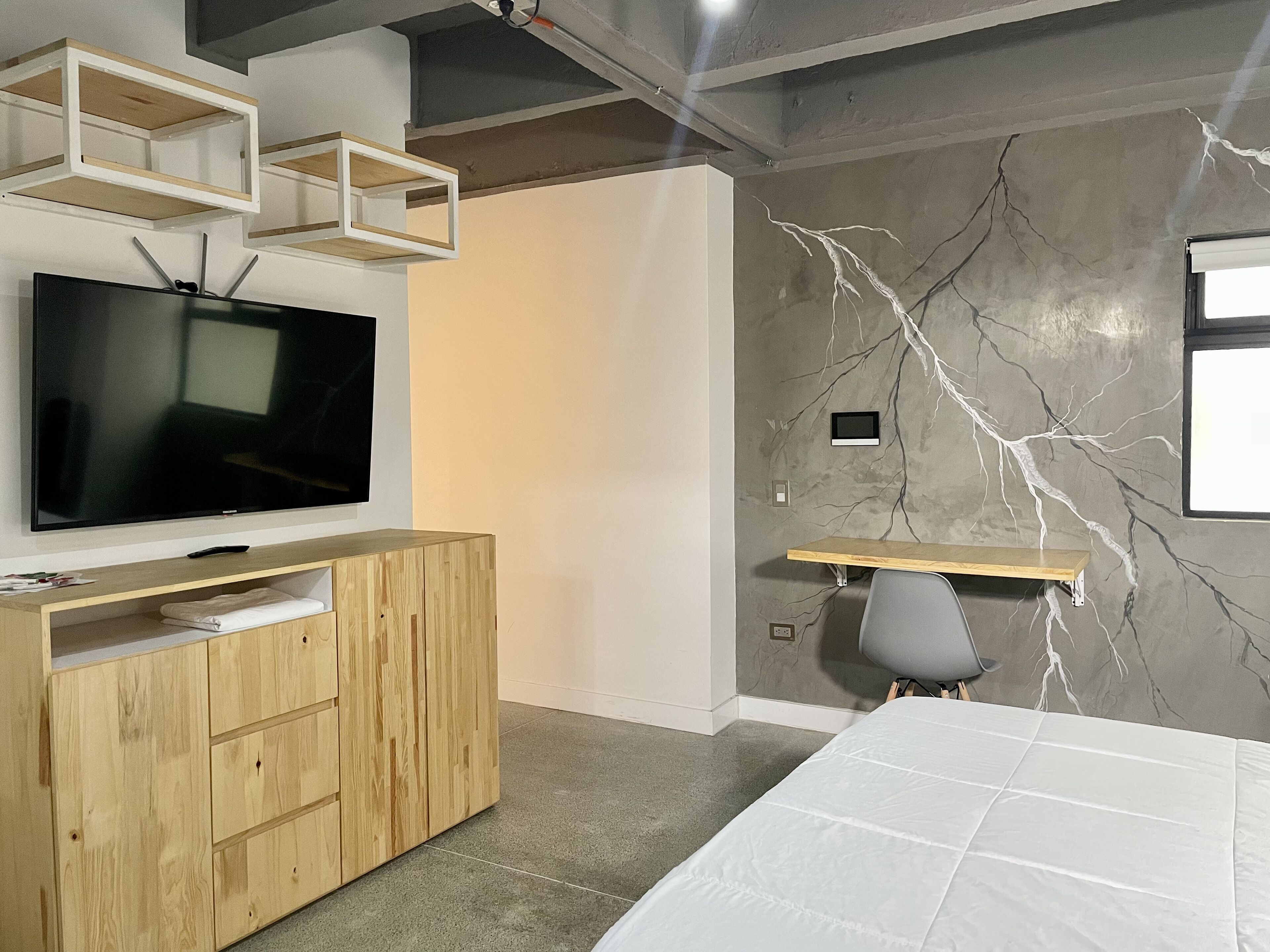 Quarto moderno com televisão de tela plana grande, mobiliário de madeira, parede com padrão marmorizado e uma cama.