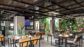 A restaurant with high ceilings, exposed beams, and tropical murals. Tables are set with chairs and centerpieces. - Edificio Helena (Medellín)