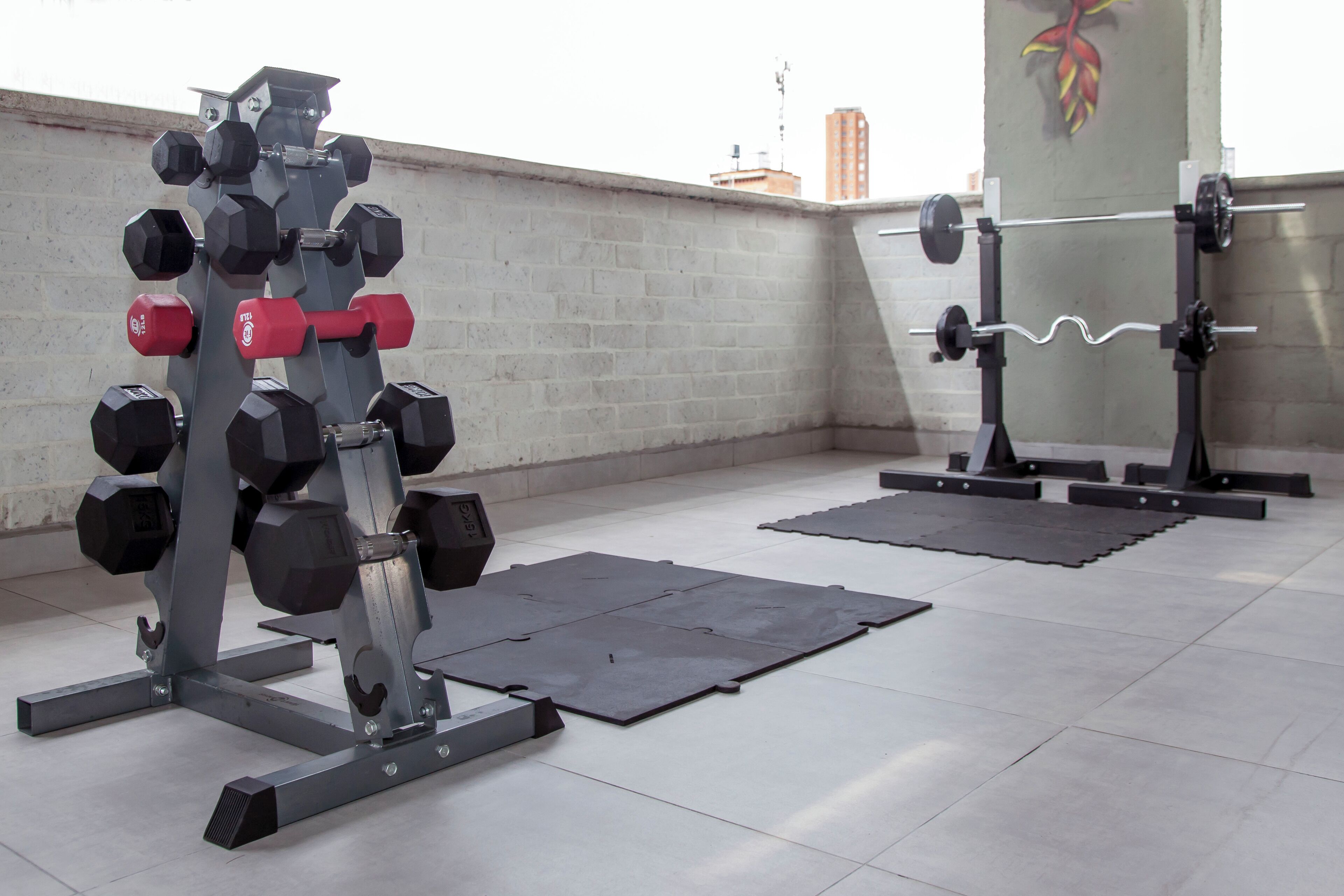 A gym with weightlifting equipment, including dumbbells and a barbell, on a tiled floor with mats.