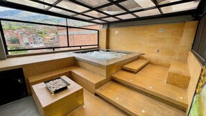 A modern spa area with a hot tub, seating, and a view of a hillside village. - Edificio Helena (Medellín)