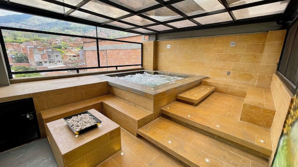 Un espace spa moderne doté d’un jacuzzi, de coins salon et offrant une vue sur un village perché sur une colline.
