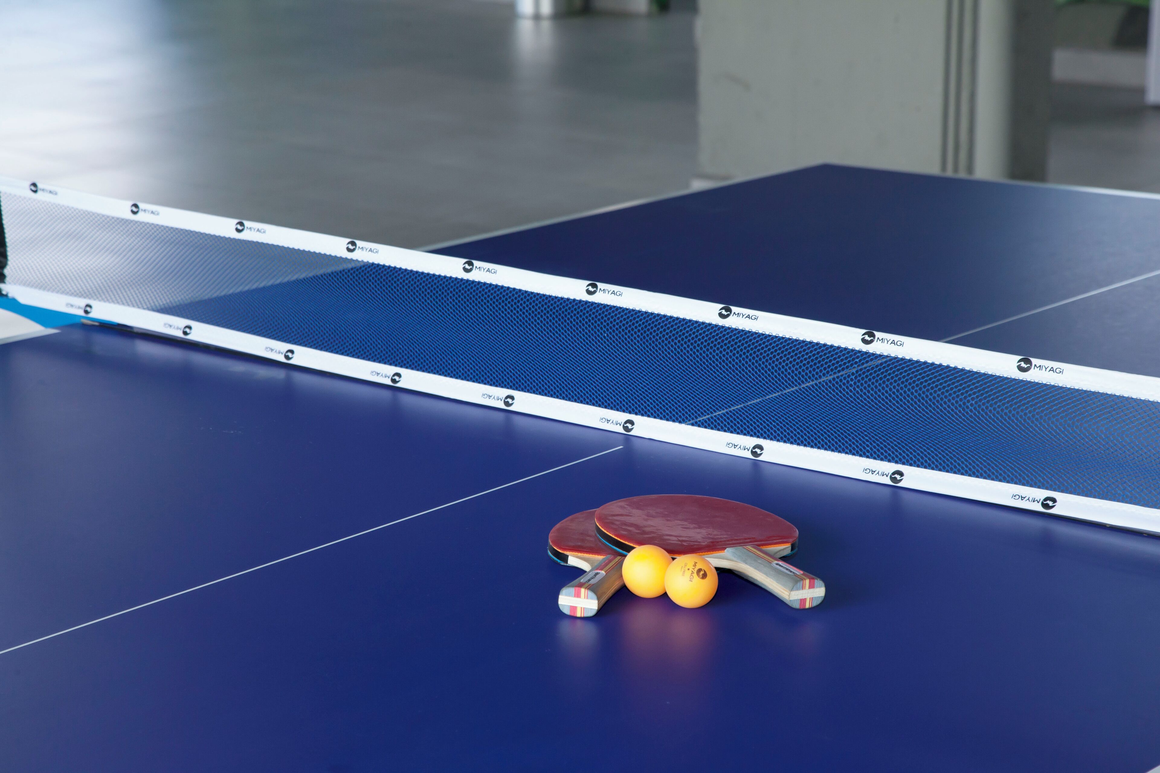 A table tennis table with a net, two paddles, and three balls.