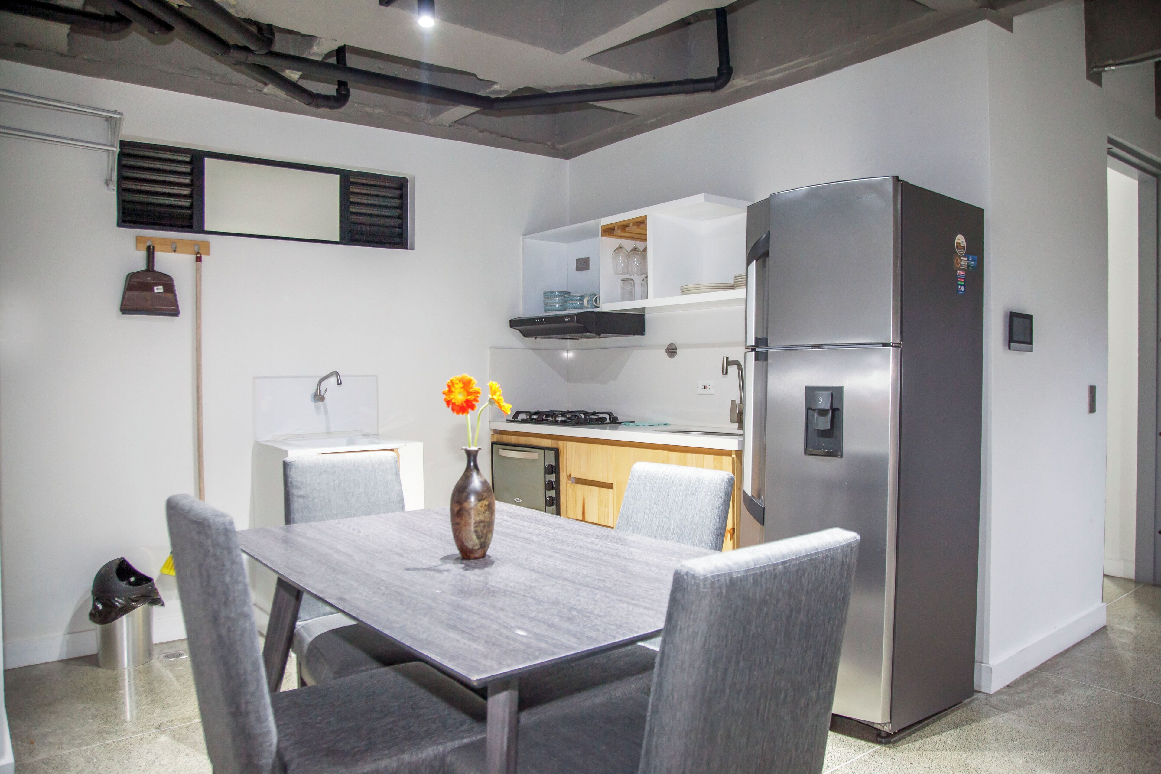 A compact kitchen with a built-in refrigerator, a dining table with chairs, and a vase with flowers.