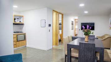 Una cocina moderna con microondas, estufa y armarios de madera. Cuenta con una zona de comedor con mesa y sillas, y un televisor montado en la pared.