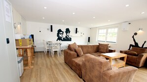 A spacious living room with a brown sofa set, a wooden coffee table, and a white dining table.