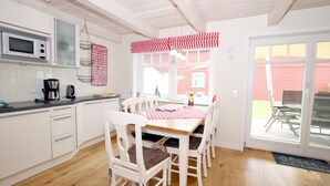 A kitchen with white cabinets, a microwave, and a coffee maker. There is a dining table with a red and white checkered tablecloth and white chairs.