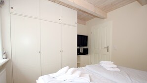 A bedroom with a bed, white wardrobe, and a television on a shelf.