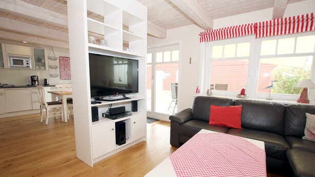 A modern living room with a flat-screen TV, a black leather sofa, and a red and white checkered tablecloth.
