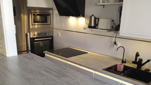 Una cocina moderna con extractor de acero inoxidable, dos hornos, microondas integrado y una encimera elegante.