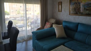 Un salón con un sofá azul, una silla, una mesa y un ventanal con cortinas ligeras.